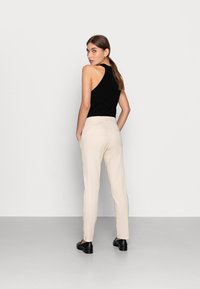 Top de alças pretas caneladas, calças creme e sapatos pretos. O top tem um design com costas nadador; as calças são justas com uma textura suave.