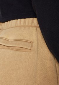 Beige trui stof met een textuurafwerking, voorzien van een elastische tailleband en een faux zakdetail. Donkere stof zichtbaar boven de tailleband.