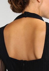 Černé šaty z vroubkované tkaniny s nízkým výstřihem na zádech, s uzávěrem na háček a oko a texturovanými akcenty podél výstřihu.