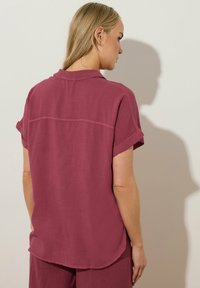 Korte mouwen, button-up shirt in stofroze, gemaakt van lichtgewicht materiaal. Beschikt over een rugnaad en opgerolde mouwen. Soepele textuur.