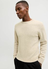 Beige wollen trui met een ronde hals, geribbelde manchetten en een gladde textuur, gecombineerd met zwarte broek.