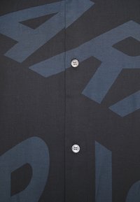 Černá košile na knoflíky s velkými tmavě modrými grafickými písmeny. Vyrobeno z tkané látky s hladkým povrchem a klasickým límcem.