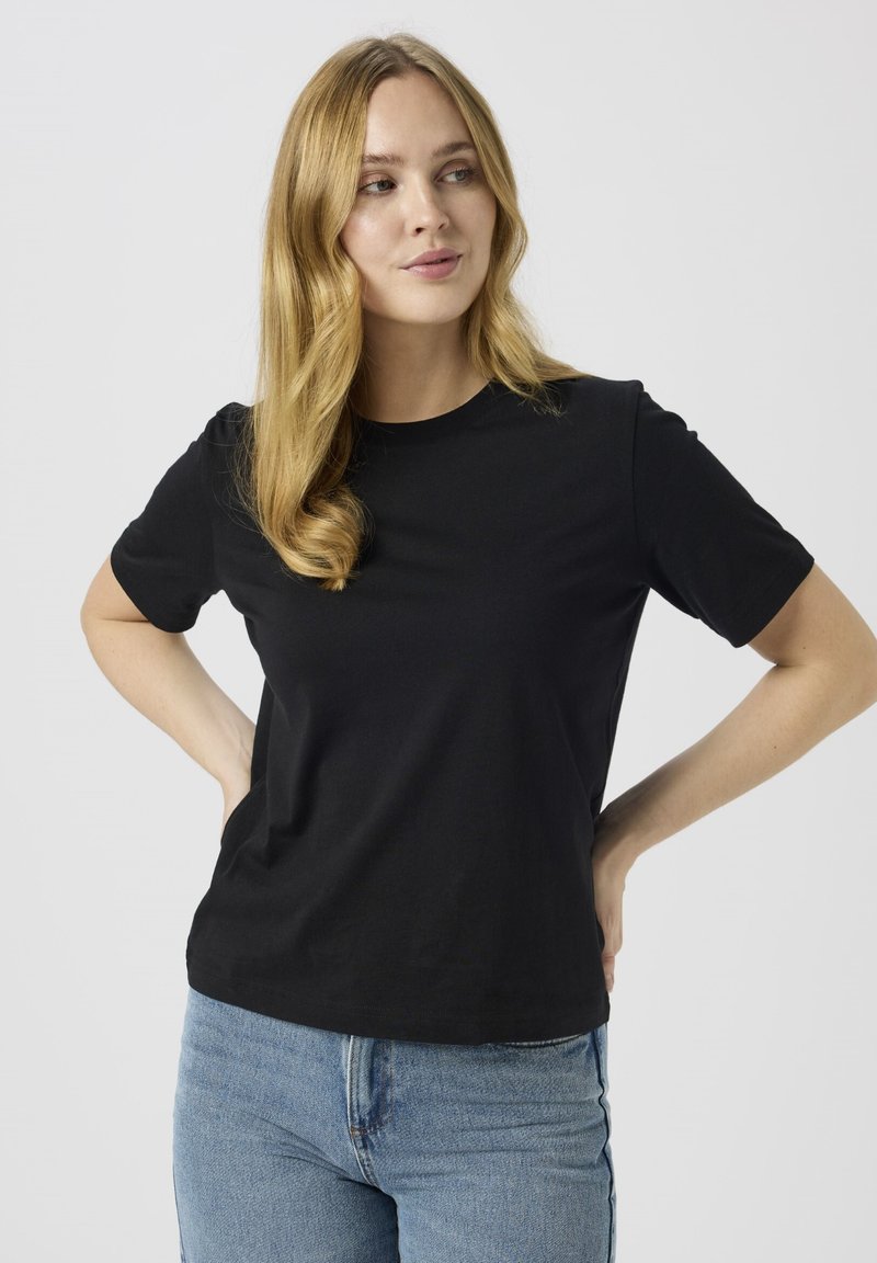 Černé tričko s krátkým rukávem z bavlny, s klasickým kulatým výstřihem a volným střihem, ve spojení se světle modrými džínami.