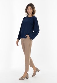 Maglietta a maniche lunghe blu navy abbinata a pantaloni tapered beige e scarpe beige con tacco a blocco, caratterizzate da un accento decorativo in oro.