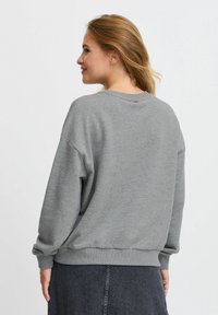 Sudadera gris de tela suave, con cuello redondo, hombros caídos y puños acanalados. Diseño simple sin patrones o acentos prominentes.