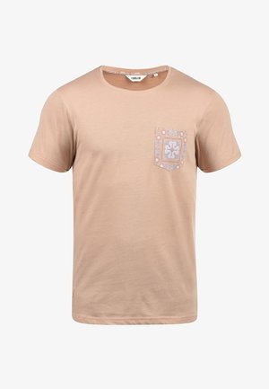 Bež pamukasta majica s kratkim rukavima i okruglim izrezom. Ima uzorak na lijevoj strani prsnog koša u plavoj i bijeloj boji.