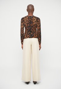 Svettr med leopardmönster i bruna och svarta nyanser, kombinerat med krämfärgade vida byxor. Slät textur med ribbade manschettdetaljer.