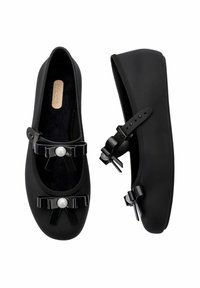 Zapatos planos negros hechos de un material suave, con un diseño de punta redonda y dos lazos negros con acentos de perlas en la parte delantera. Forro interior suave.