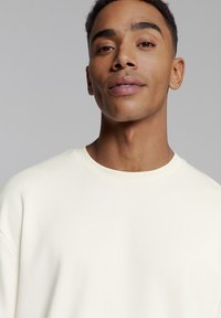 Crewneck sweatshirt in gebroken wit. Zachte, gladde textuur met verlaagde schouders en een relaxte pasvorm. Minimalistisch ontwerp, geen zichtbare patronen of accenten.