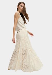 Ivory kant maxi rok, met een gelaagd ontwerp en bloemmotieven met een aansluitende pasvorm. Gecombineerd met een textuur crème tanktop.