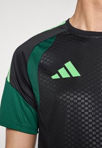 Black and green short-sleeve athletic shirt with a textured pattern, featuring reflective green Adidas logo on the chest.