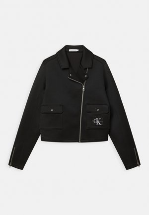 Czarna krótkia kurtka wykonana z gładkiej tkaniny, posiadająca zamek błyskawiczny z przodu, dwie naszywane kieszenie, zamki po bokach oraz naszywkę z logo po lewej stronie.