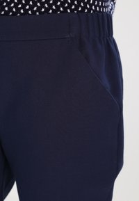 Navy blue pants featuring a soft fabric, elastic waistband, and side pocket. Smooth texture with a relaxed fit for comfort.
