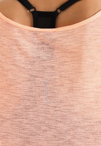 Top texturizado color durazno con un escote amplio, que muestra un diseño de tirantes negros en la espalda y detalles sutiles impresos a lo largo de la tela.