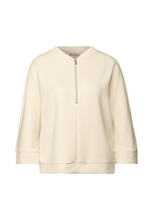 Pull en beige clair avec un col haut et une fermeture éclair à l'avant. Fabriqué en tissu doux, il présente des manches 3/4 amples et une coupe décontractée.