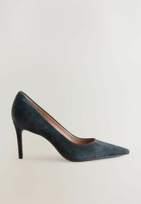 Temno sivi nubuk salonar z visoko peto z uskim stiletto peto in koničastim prstom. Notranjost ima gladek bež podstavek.