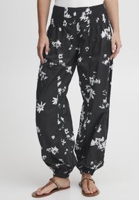 Svarta blommiga byxor gjorda av lättviktsmaterial, med ett smockat midjeband och vadderade ärmslut, med ett vitt blommönster över hela plagget.