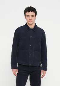 Μπλε σκούρο σακάκι από κορδούρο με κούμπωμα με κουμπιά, δύο μεγάλες μπροστινές τσέπες και κλασικό γιακά. Το ύφασμα έχει υφή με ανάγλυφη επιφάνεια.