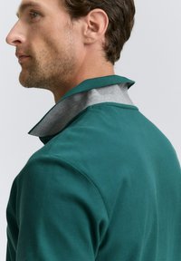 Teal polo skjorte med grå krave, med et tekstureret stof og en moderne pasform. Synlige syninger langs sømmen og kravekanterne.