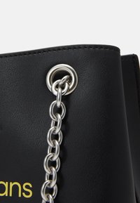 Black faux leather bag with a silver chain and grommet detail. The surface has a textured finish, and a branded logo is visible.