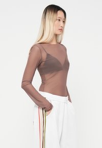 Brown sheer long-sleeve top with a fitted design. Paired with white sweatpants featuring multicolored stripes along the sides.