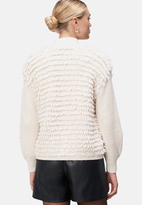 Chunky crèmekleurige trui met een gestructureerde, verhoogde stof op de rug, voorzien van gebreide mouwen en een aansluitende zoom. Gecombineerd met zwarte shorts.