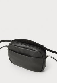 Μαύρη δερμάτινη τσάντα χιαστί με λεία υφή, διαθέτοντας κλείσιμο με φερμουάρ και λεπτό σχέδιο. Περιλαμβάνει αποσπώμενο λουρί.