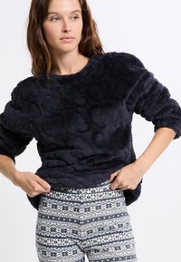 Marinblå fleece-tröja med texturerat hjärt-mönster, rund halsringning och långa ärmar, i kombination med mönstrade leggings i marinblå och krämfärg.