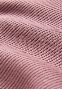 Textielstof in zacht roze met een ribbelstructuur. Golfachtige lijnen creëren een subtiel patroon, met gladde, gelijkmatige steken en een lichte glans.