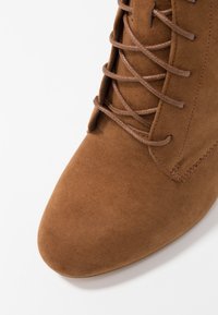 Brun mockaskinnankelboot med spetsig tå och snörningsdesign. Strukturerad ovandel, förstärkt sömnad och en slät yta.