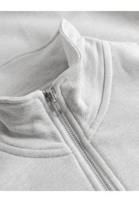 Grijze zip-up sweatshirt met een zachte, gevlekte stof, hoge kraag en zilveren rits, gericht op eenvoud en comfort.