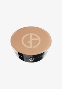 Compact cosmétique rond avec un couvercle beige arborant un logo, base noire et texture lisse. Diamètre d'environ 10 cm.