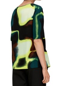 Koszulka z krótkim rękawem z abstrakcyjnym wzorem w kolorach zielonym, czarnym i brązowym. Wykonana z gładkiego materiału, ma luźny krój i okrągły dekolt.