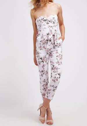 Strapless bloemenjumpuit in het wit met roze bloemen, met een aansluitend lijfje, ceintuur in de taille en taps toelopende pijpen. Gladde stof met een zachte textuur.