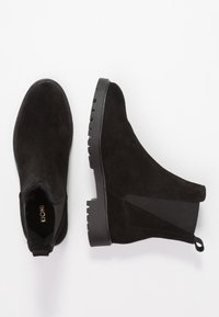 Botas Chelsea de ante negro con paneles laterales elásticos y lengüetas de tirón, con suelas de goma robustas, exhibidas sobre un fondo blanco.