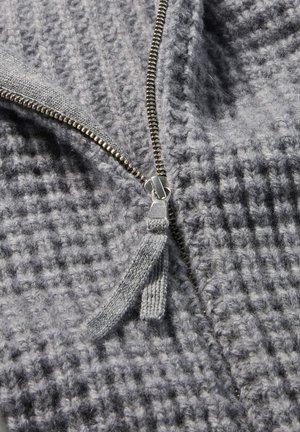 Grau gestrickte Strickjacke mit einem strukturierten Muster, metallischen Reißverschluss und Stofflasche. Das Material wirkt weich und gemütlich.