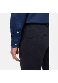 Temno modra srajca z dolgimi rokavi in gumbastimi manšetami, v kombinaciji s temno modrimi hlačami z žepom in teksturirano površino.