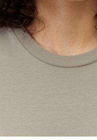 Jasnoszary t-shirt z prążkowanym dekoltem, gładką fakturą i dopasowanym krojem, z minimalnym przeszyciem i bez widocznych wzorów.