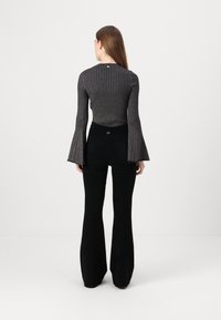 Top long-sleeve côtelé gris avec des manches évasées, associé à un pantalon noir évasé présentant un accent doré au niveau de la taille.