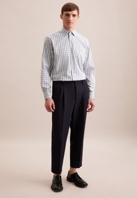 Camicia a quadri blu chiaro e bianca con colletto a punta, abbinata a pantaloni scuri a vita alta e scarpe nere con lacci.