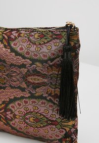 Pochette en tissu décorative avec un motif floral multicolore complexe, fermeture éclair dorée et pompon noir sur fond clair.