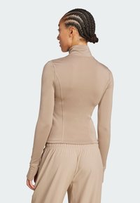 Eng anliegendes langärmeliges Oberteil aus glattem, dehnbarem Stoff in hellem Beige mit hohem Kragen und Nahtdetails, kombiniert mit Hosen mit elastischem Bund.