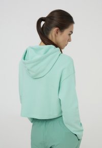 Hoodie verde menta tagliata, realizzata in materiale morbido con cappuccio, con maniche lunghe e vestibilità comoda, abbinata a pantaloni coordinati.