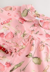 Ružičasti pamučni odjevni predmet s ovratnikom, ukrašen cvjetnim uzorkom s gljivama i miševima. Ima kopčanje na gumbe i skupljene detalje.