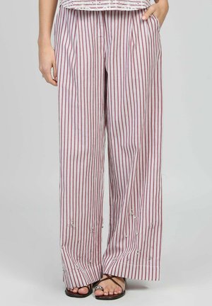 Femme portant un pantalon ample à rayures verticales rouges et blanches avec de petites perles décoratives près de l'ourlet, associé à des sandales plates marron.