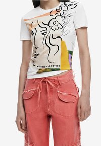 Bílý bavlněný tričko s barevným abstraktním designem obsahující liniovou kresbu a květinové akcenty. V kombinaci s vybledlými růžovými šortkami ve stylu cargo s kapsami.