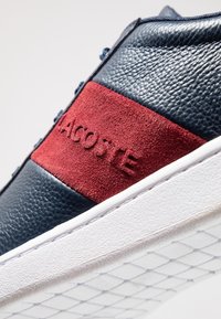 Marinblå lädersneakers med ett rött mockaband, utrustade med ett präglat logotyp, vit gummisula och texturerad ovandel för bättre grepp.