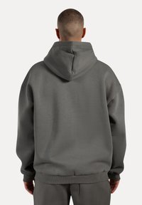 Felpa con cappuccio grigia dalla vestibilità rilassata, con polsini e orlo a coste, caratterizzata da una texture liscia e un peso consistente del tessuto.