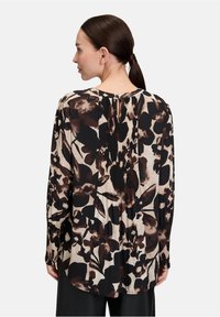 Blusa a maniche lunghe in beige con stampa floreale scura, caratterizzata da un retro plissettato e dettaglio a chiave sullo scollo. Tessuto dalla trama liscia.