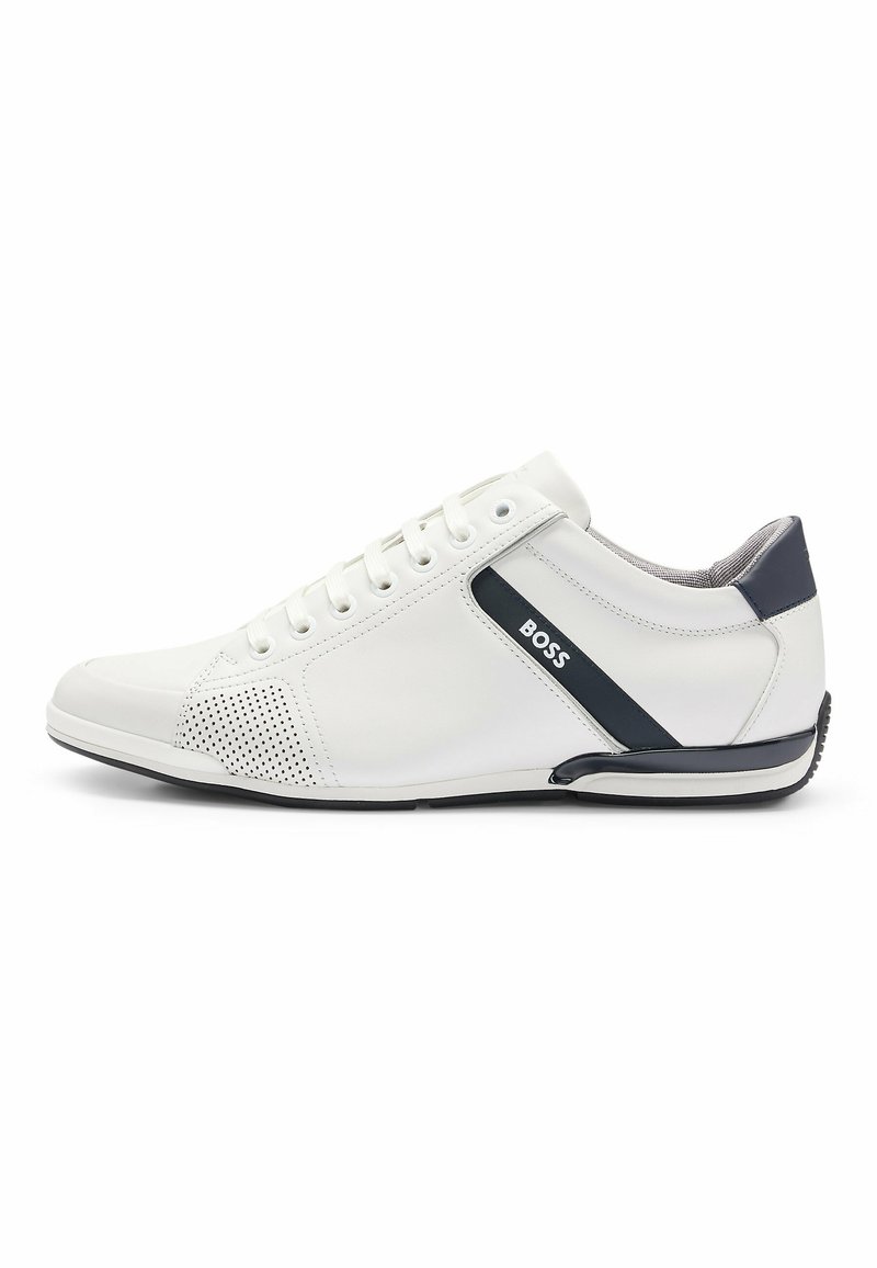 Zapatilla de cuero blanca con acento en azul marino, diseño perforado en el lateral, punta redonda, seis ojales y suela contrastante para mayor tracción.